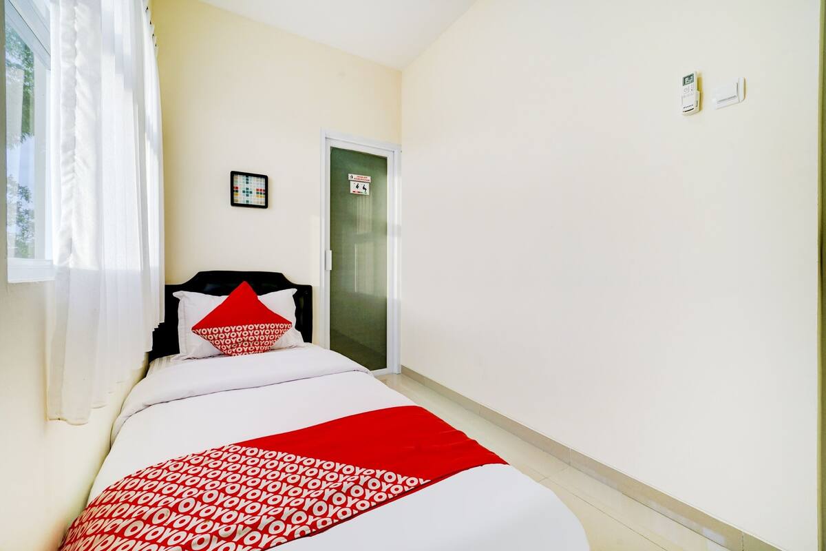 A hotel room with a bed, a door, a window with curtains, and a wall-mounted thermostat.