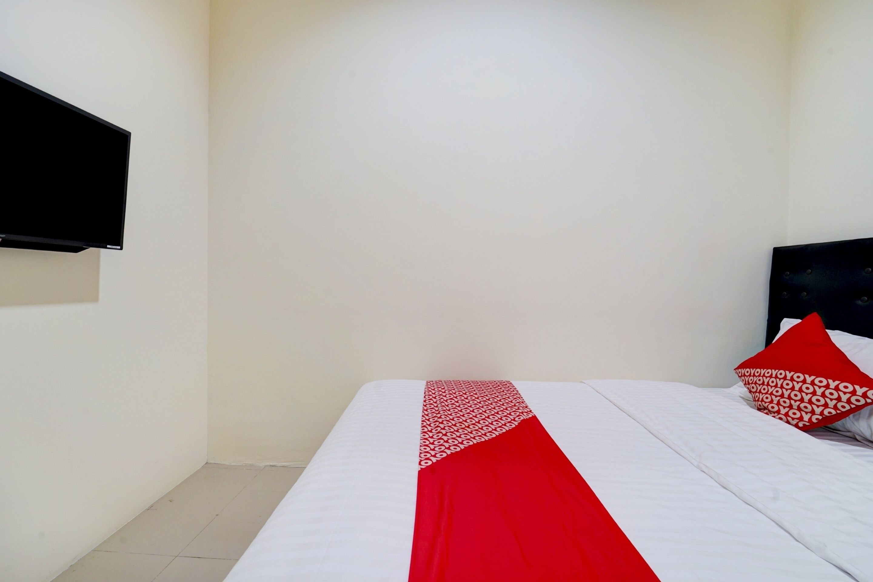 A hotel room with a bed, a TV mounted on the wall, and a red and white patterned bedspread.