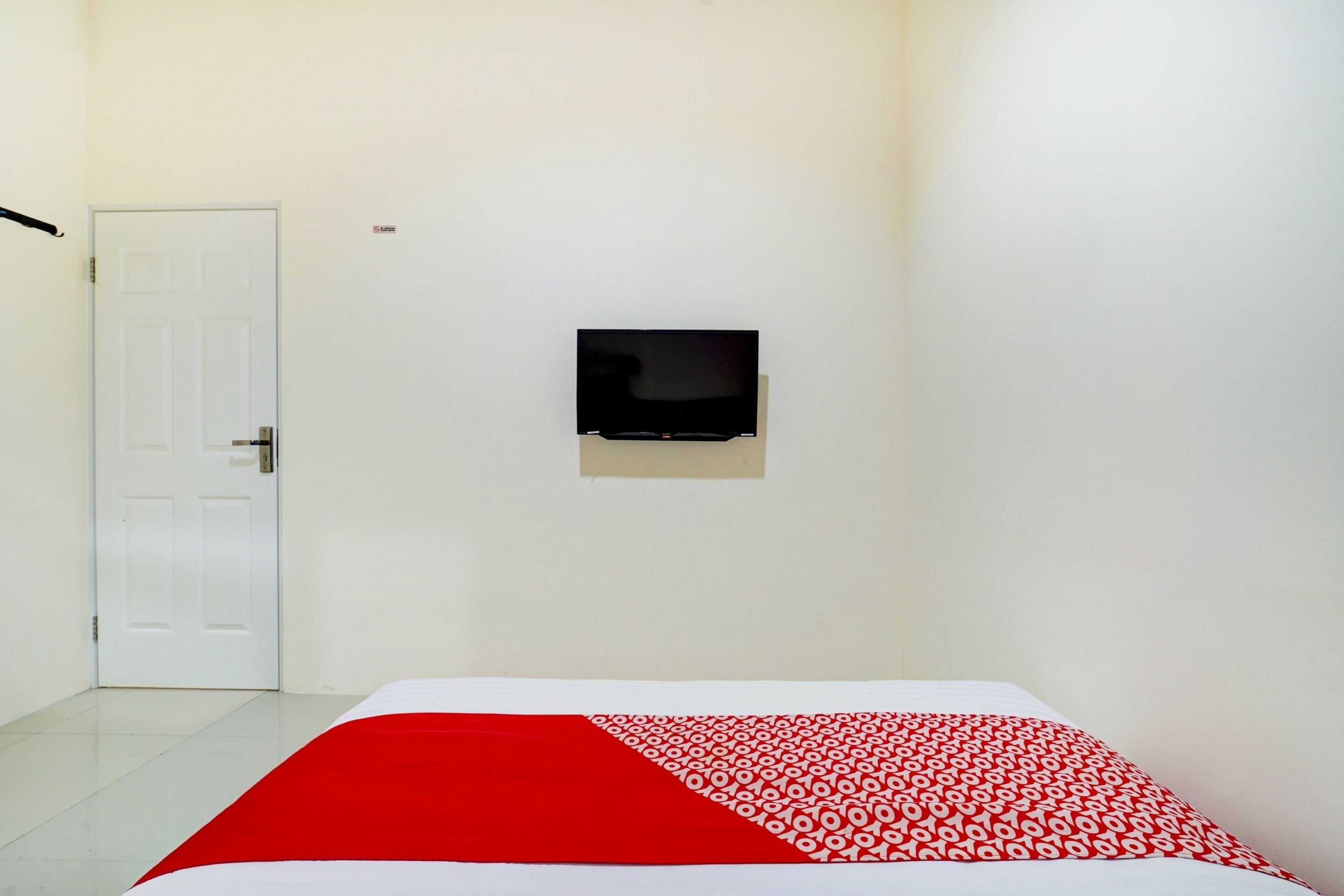 A hotel room with a bed, a television mounted on the wall, and a door.