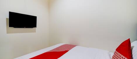 A hotel room with a bed, a flat-screen TV mounted on the wall, and a red and white patterned pillow.