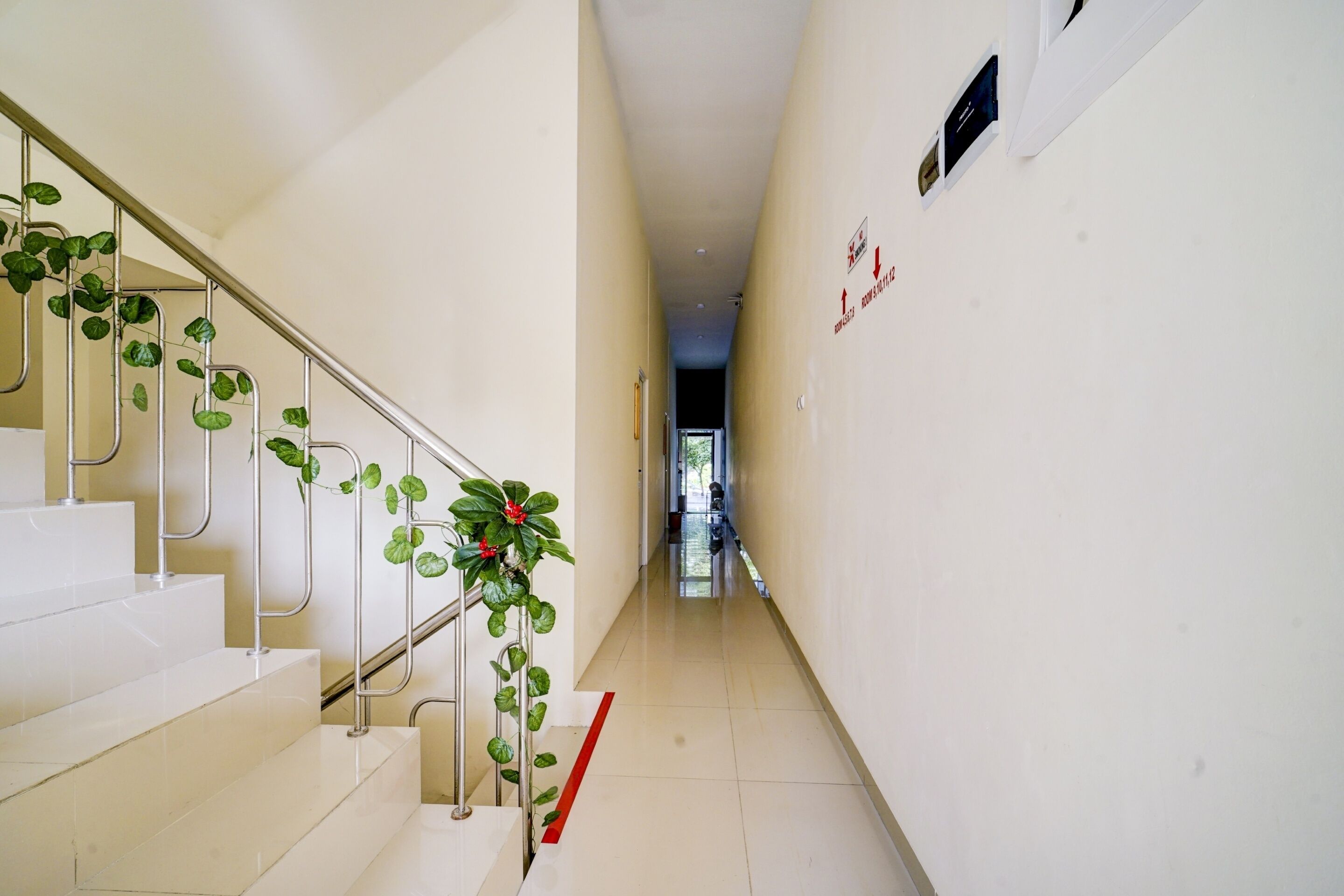 Un couloir propre et moderne, avec un escalier sur la gauche, une ligne rouge sur le sol et une porte au fond.
