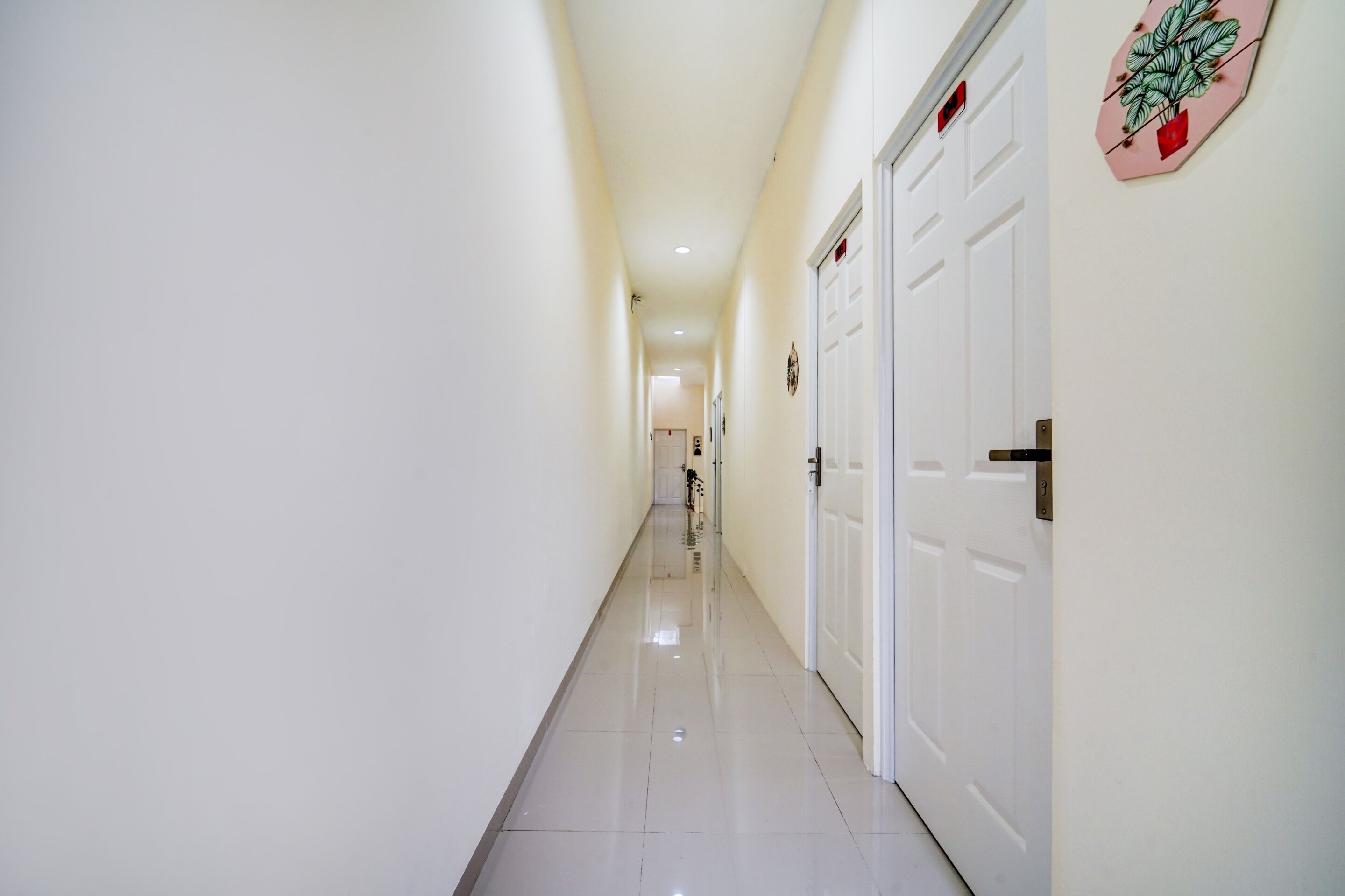 Corredor com paredes e portas brancas, que dá acesso a um quarto.