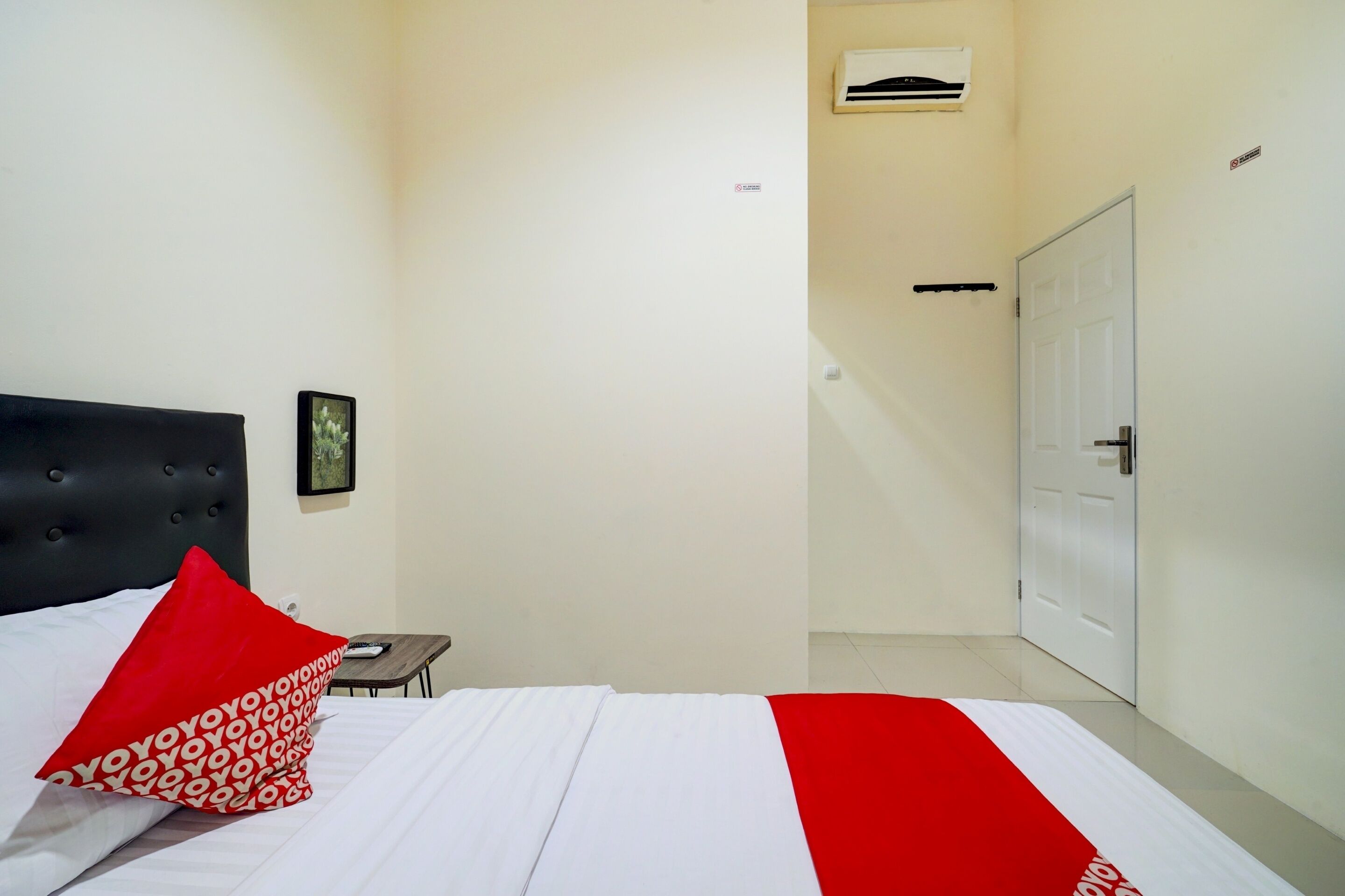 A hotel room with a bed, a nightstand, a wall-mounted air conditioner, and a door.