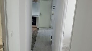 Un pasillo estrecho con suelo de madera claro, paredes blancas y una puerta que da a una zona de cocina.