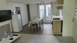 Un espacio habitable compacto con comedor, kitchenette y televisor montado en la pared.