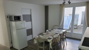 Cocina compacta con microondas y refrigerador, una mesa de comedor con sillas y un ventanal corredizo que da a un espacio exterior.