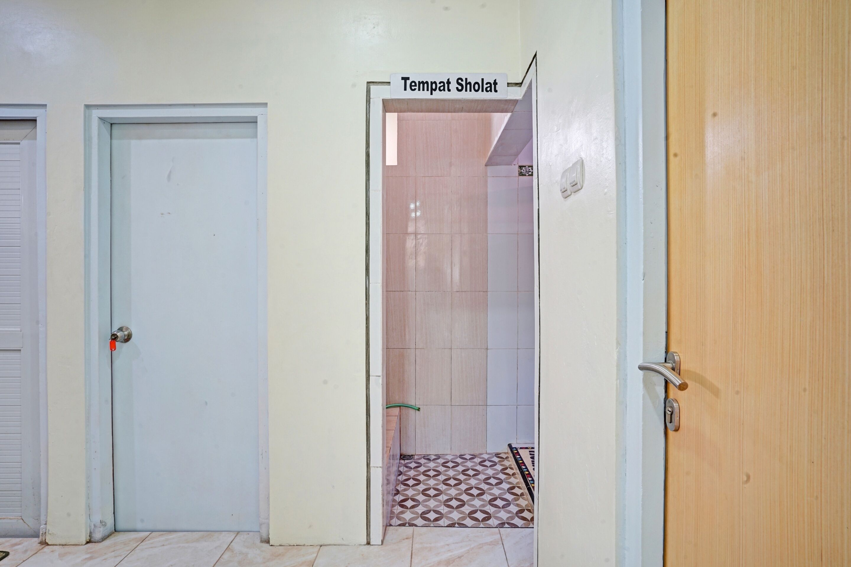 A hallway with two doors, one labeled "Tempat Sholat" leading to a prayer room, and another closed door.