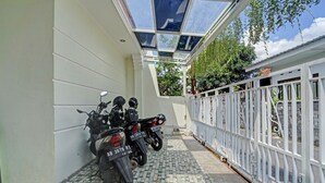 Un espace extérieur abrité avec deux motos garées contre un mur blanc, un sol carrelé et une clôture métallique blanche.