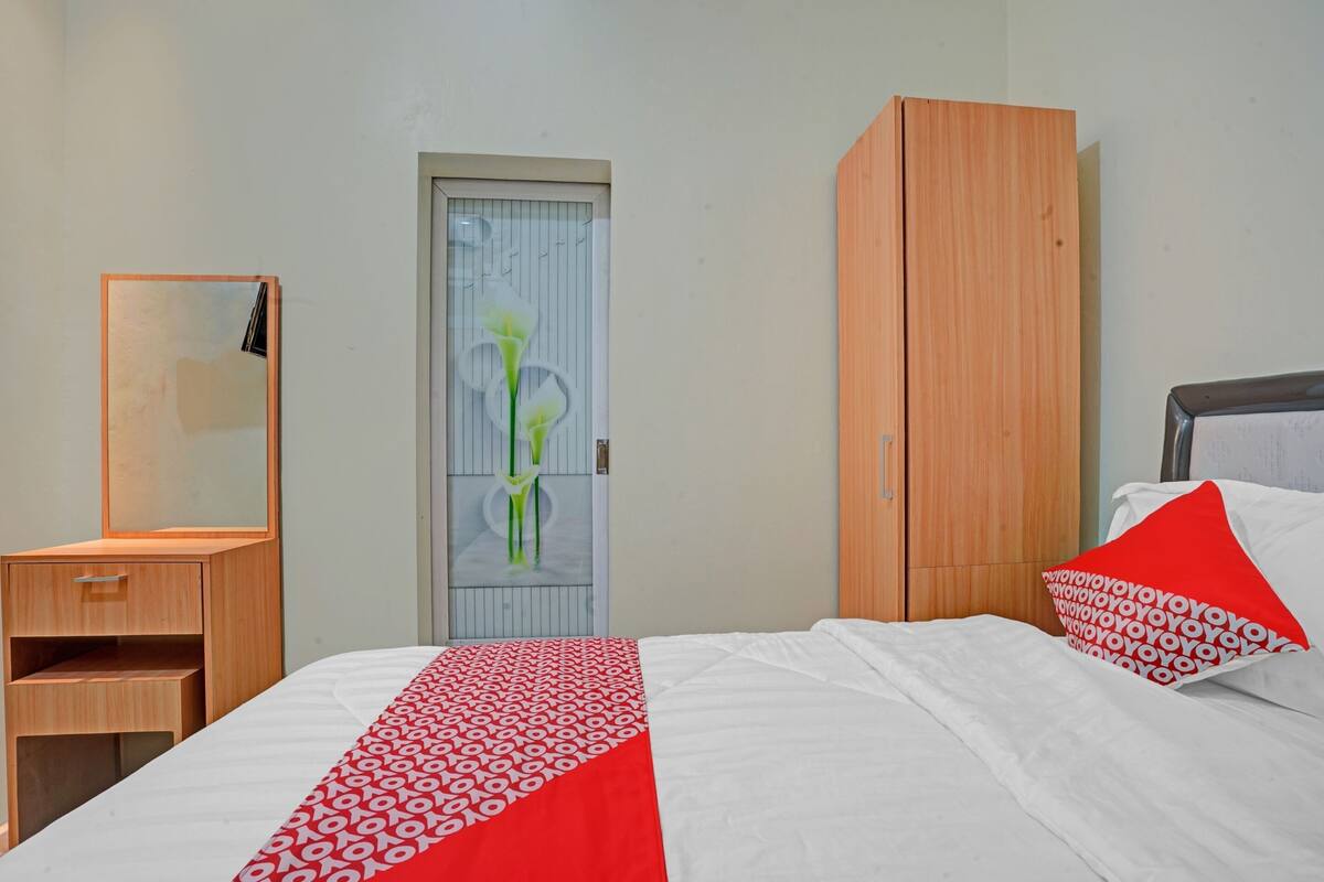 Une chambre à coucher comprenant un lit, une armoire en bois, un miroir et une porte ornée d’un panneau décoratif.