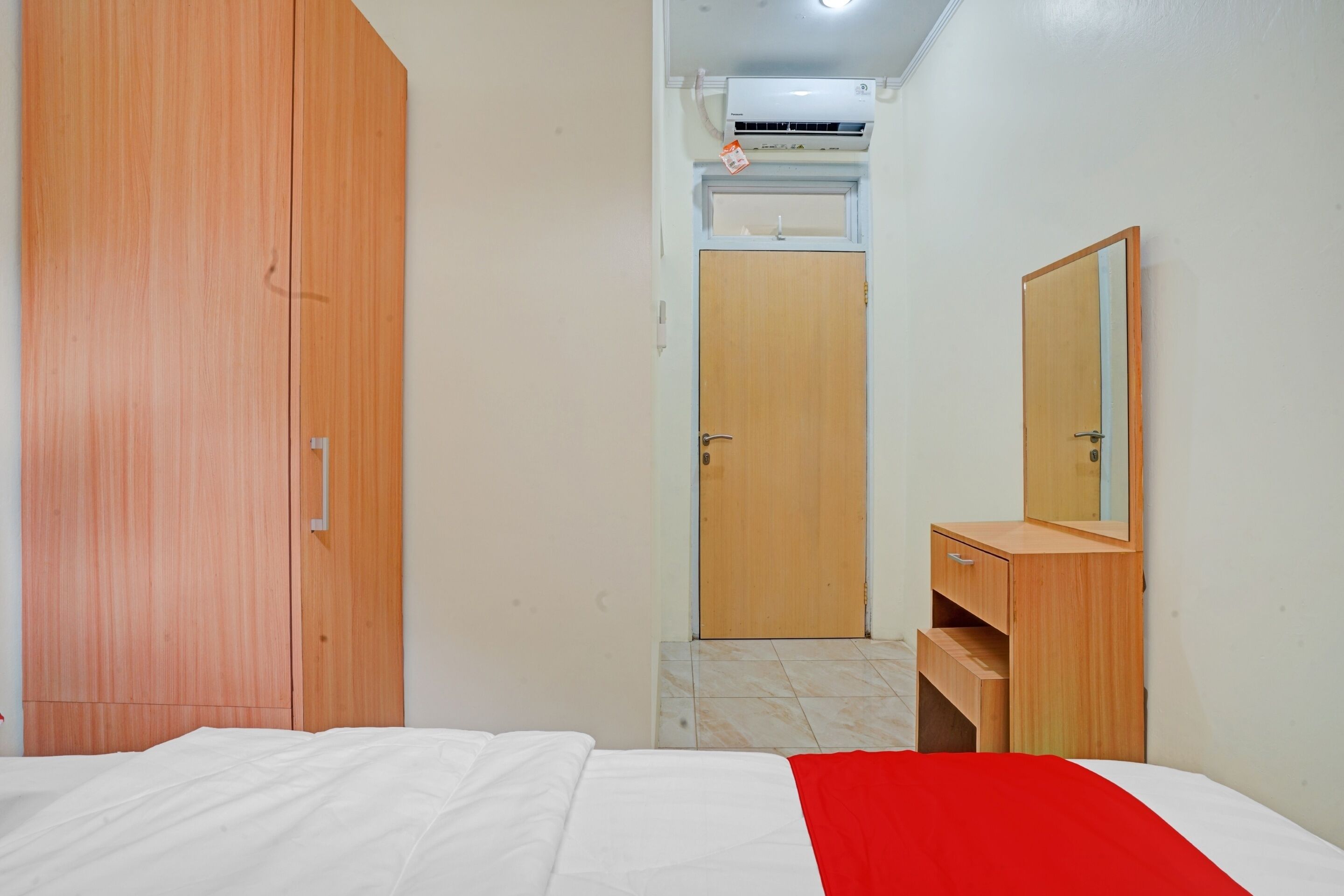 A bedroom with a bed, a wooden wardrobe, a dresser with a mirror, and a door leading to another room.