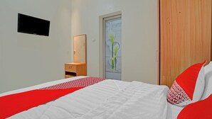 Une chambre à coucher comprenant un lit, une armoire en bois, un téléviseur fixé au mur et une porte avec un panneau de verre.
