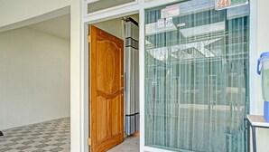 L’entrée d’un hôtel, avec une porte en bois, une fenêtre en verre ornée de rideaux et un sol carrelé.