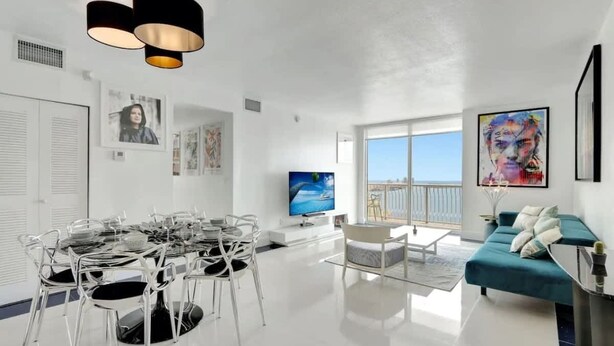 A modern living room with a dining area, large windows, and artwork on the walls. - 3BR Penthouse with European Flair & Amazing Views (Miami)