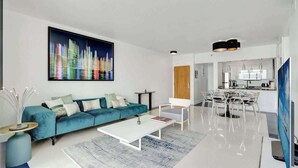 A modern living room with a teal sofa, a white coffee table, and a cityscape painting on the wall. - 3BR Penthouse with European Flair & Amazing Views (Miami)