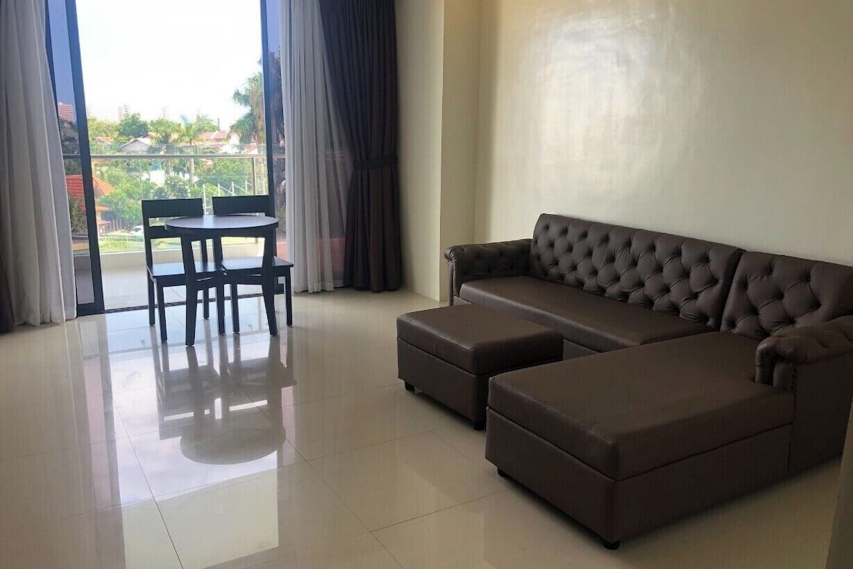 Una sala de estar con un sofá modular, una mesa de comedor con sillas y vistas a través de una puerta de cristal.