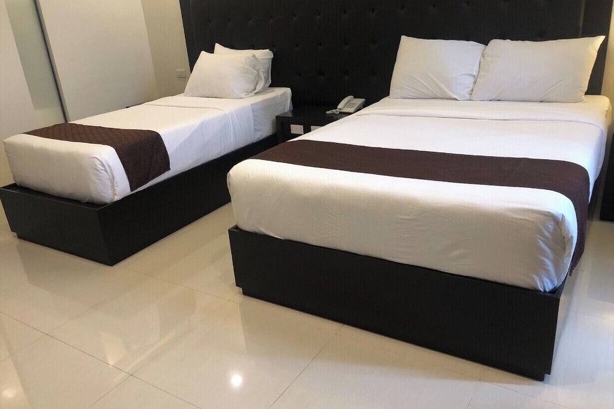 Habitación de hotel con dos camas, cada una con cabecera oscura y ropa de cama blanca.