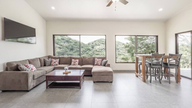 A modern living room with a sectional sofa, a coffee table, and a dining area with chairs. - Journeys End-stunning Views In Gated Community (Atenas)