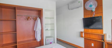 Una habitación de hotel con una cama, un armario de madera, un televisor y un ventilador de pared.