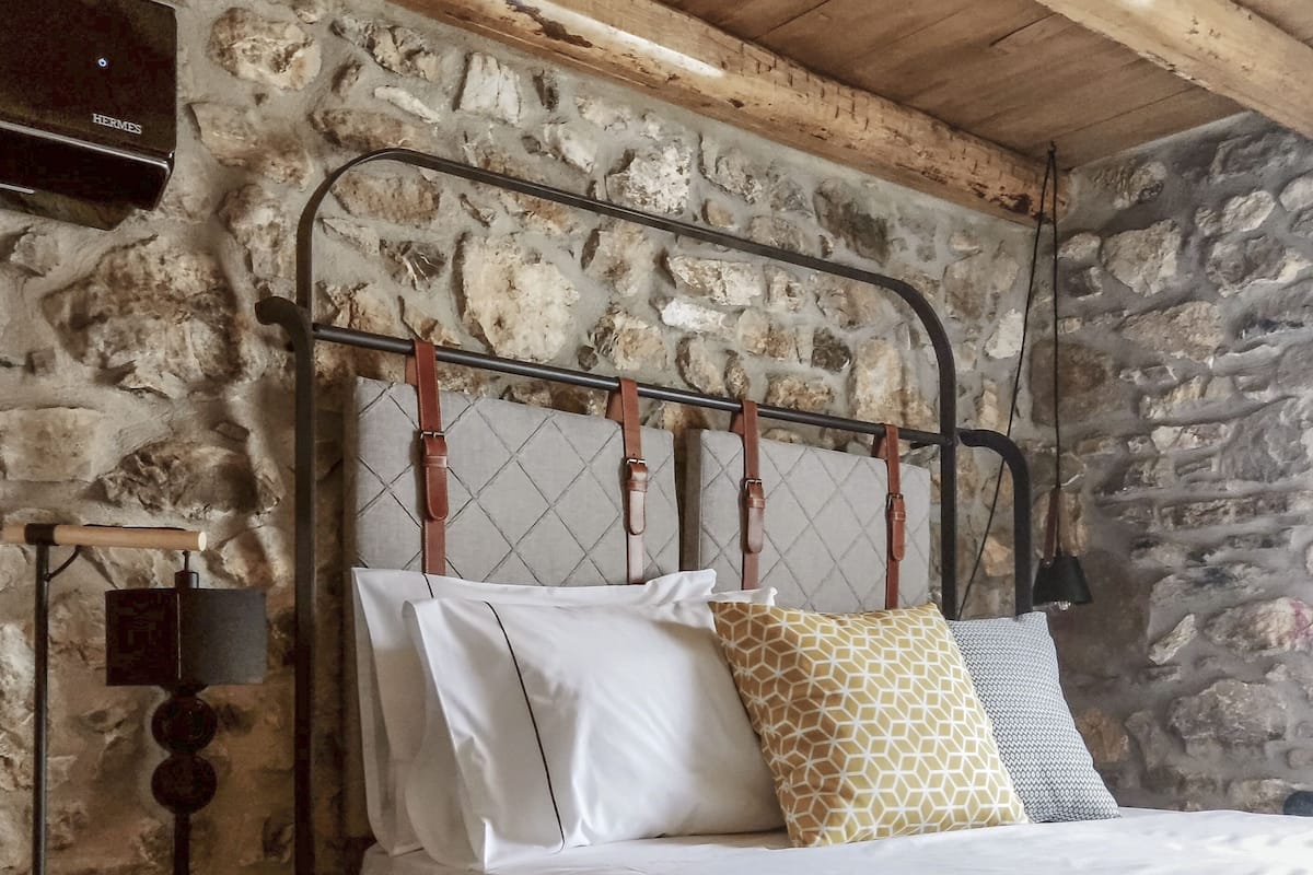 Ein Schlafzimmer mit Steinwand, Metall-Kopfteil, Nachttisch aus Holz und einer Lampe.