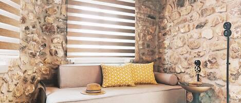 A stone-walled room with a sofa, a patterned cushion, a woven vase, and a small table with a decorative item.