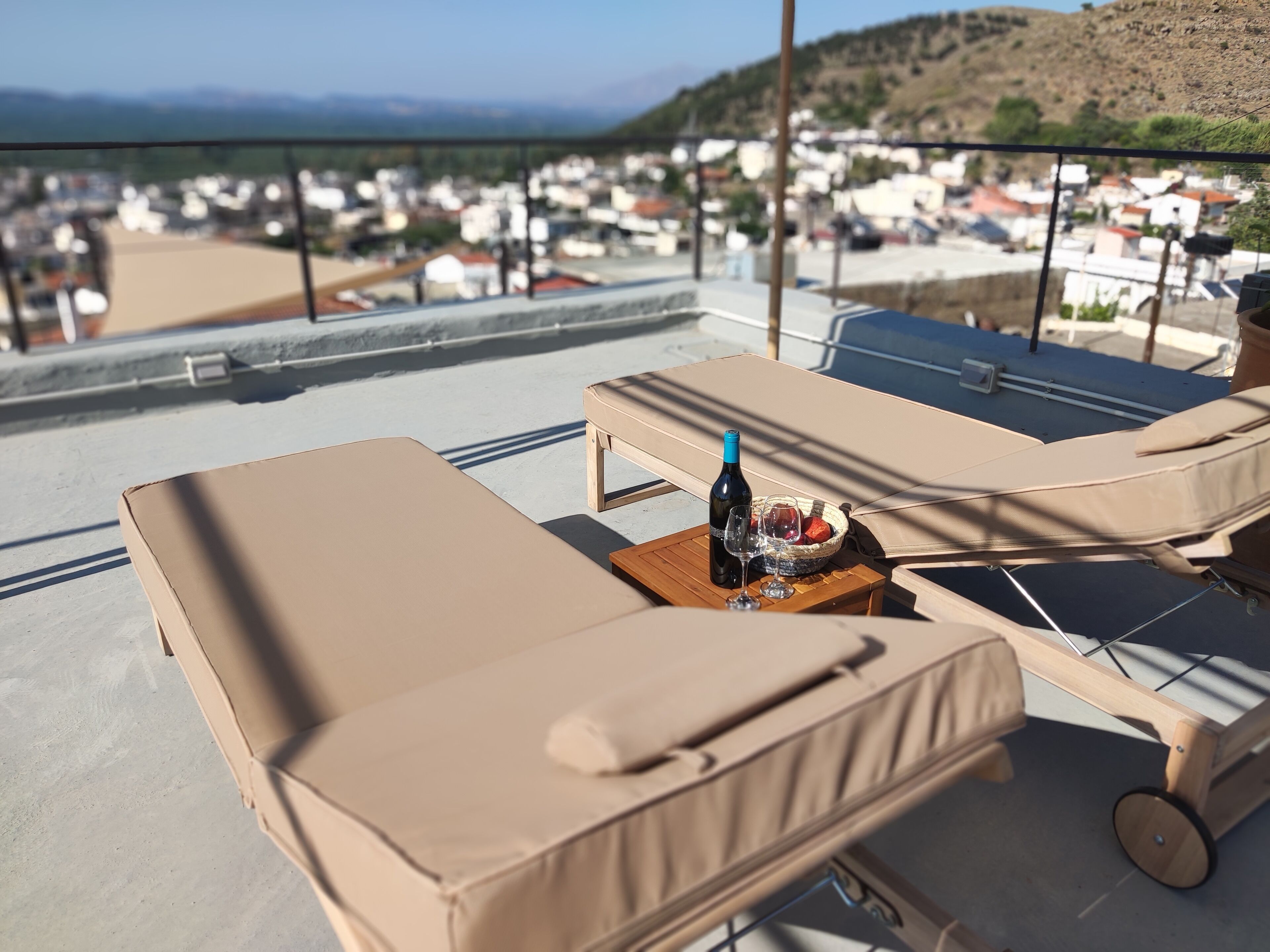 Una terrazza luminosa con due poltrone, un tavolo con una bottiglia e dei bicchieri, e vista su una località costiera.