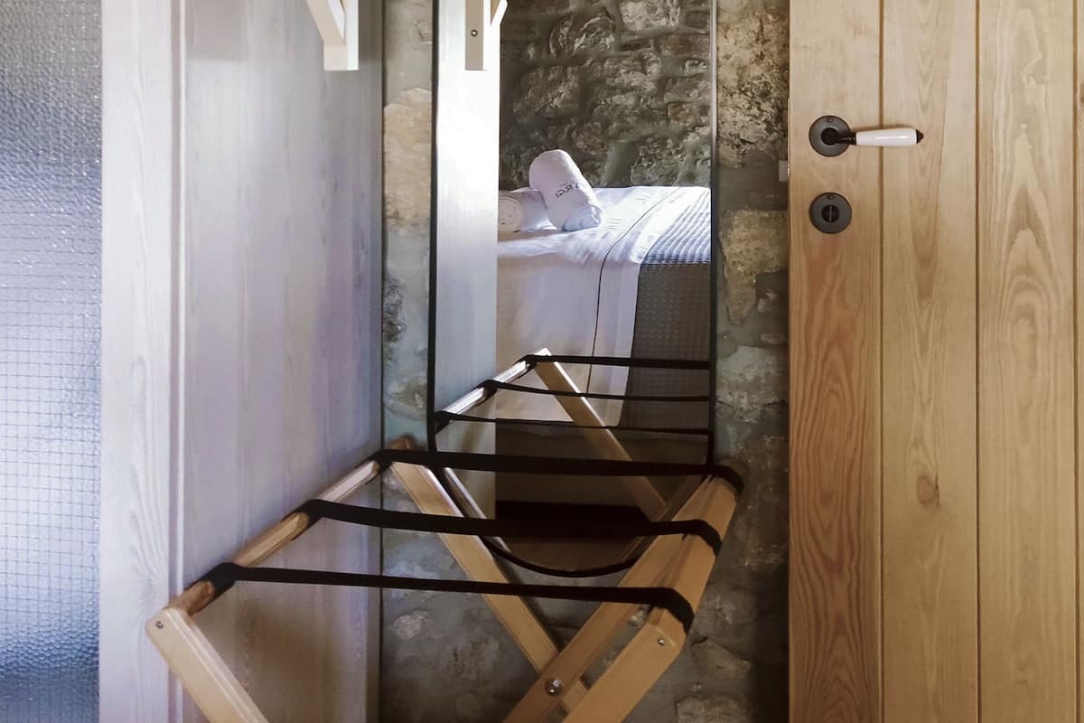 Ein Zimmer mit einem Bett, einer Holztür, einem Spiegel und einer Metallbank.