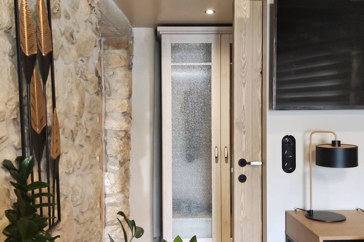 Ein modernes Interieur mit einer Steinwand, einer Holztür mit Milchglas, einer schwarzen Schreibtischlampe und einem Topfpflanzen.