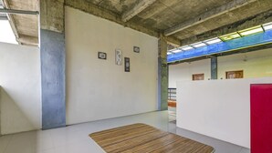 Een ruime kamer met een groot houten vloermat, witte wanden en een zichtbaar plafond met betonnen balken.