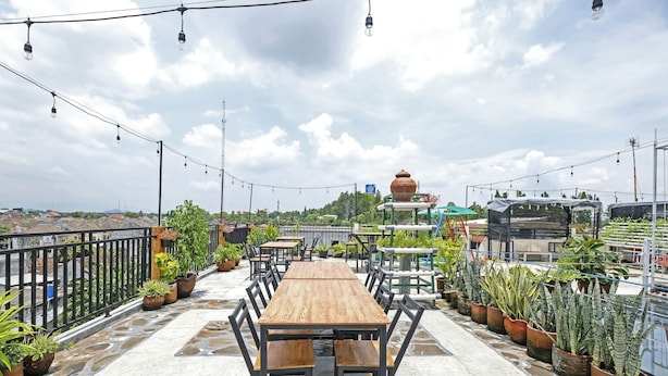 Een terras op het dak met een houten tafel en stoelen, omringd door potplanten en lichtjes.