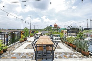 A rooftop terrace with a wooden table and chairs, surrounded by potted plants and string lights. - Hotel O Dangau Datuk Guesthouse (Sleman)