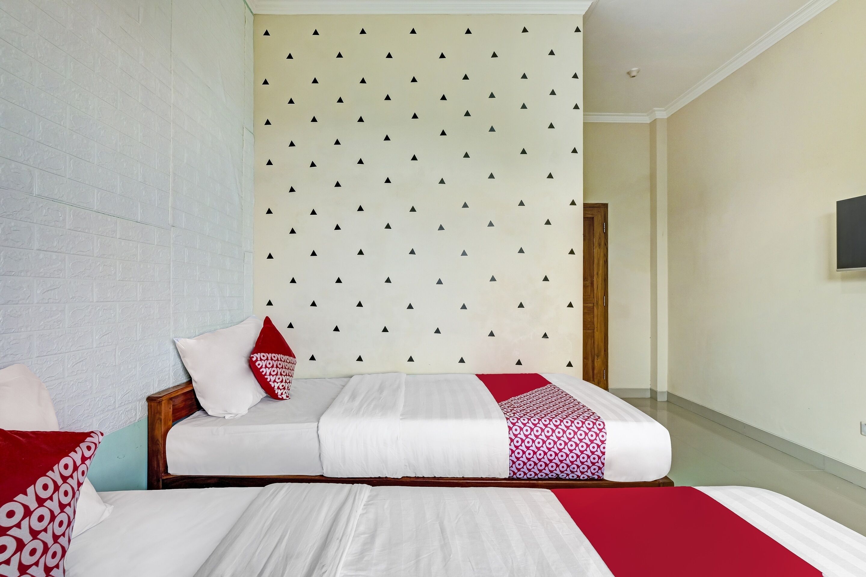 A hotel room with a bed, a wooden headboard, a patterned wall, and a television on the wall.