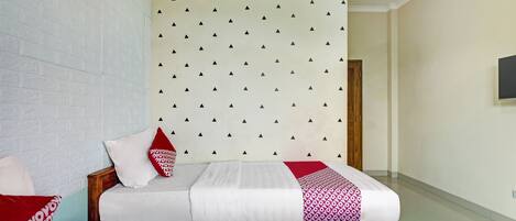 A hotel room with a bed, a wooden headboard, a patterned wall, and a television on the wall.