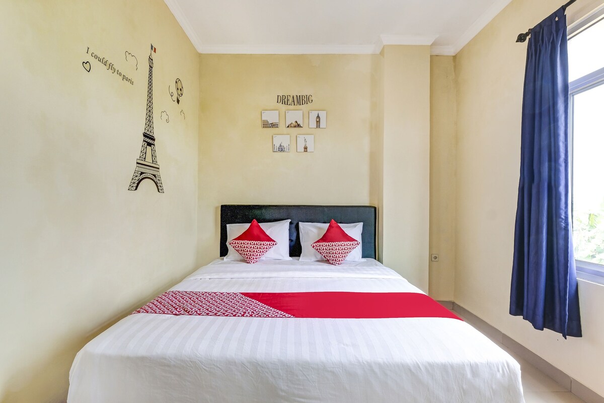 A neatly made bed with white and red bedding, a headboard with red and white pillows, and a wall with a picture of the Eiffel Tower and the word "DREAMBIG".