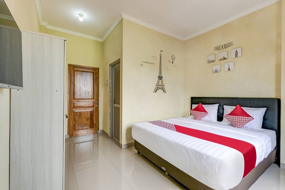 Ein Hotelzimmer mit einem Bett, einem Kleiderschrank, einer Tür und einer Wand mit einem Bild des Eiffelturms und weiteren Abbildungen.