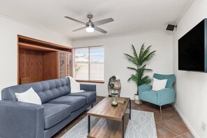 A living room with a blue sofa, teal armchair, wooden coffee table, and a ceiling fan.