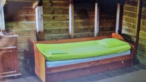 Una habitación pequeña y cerrada con una cama individual, un banco de madera y una pequeña mesa.
