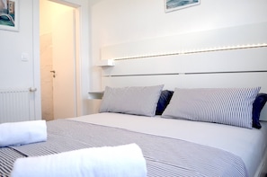 Ett hotellrum med en säng, en dörr och en sänggavel med inbyggd belysning.