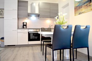 Una cocina moderna con armarios blancos, una estufa y una cafetera. Hay tres sillas alrededor de una mesa.