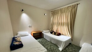 A small, clean room with two single beds, a wooden nightstand, a small table, and a window with curtains. - Hotel Camp De Base (Namche Bazar)