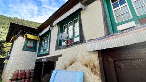 A traditional building with a stone-paved courtyard, a satellite dish, and a corrugated metal roof. - Hotel Camp De Base (Namche Bazar)