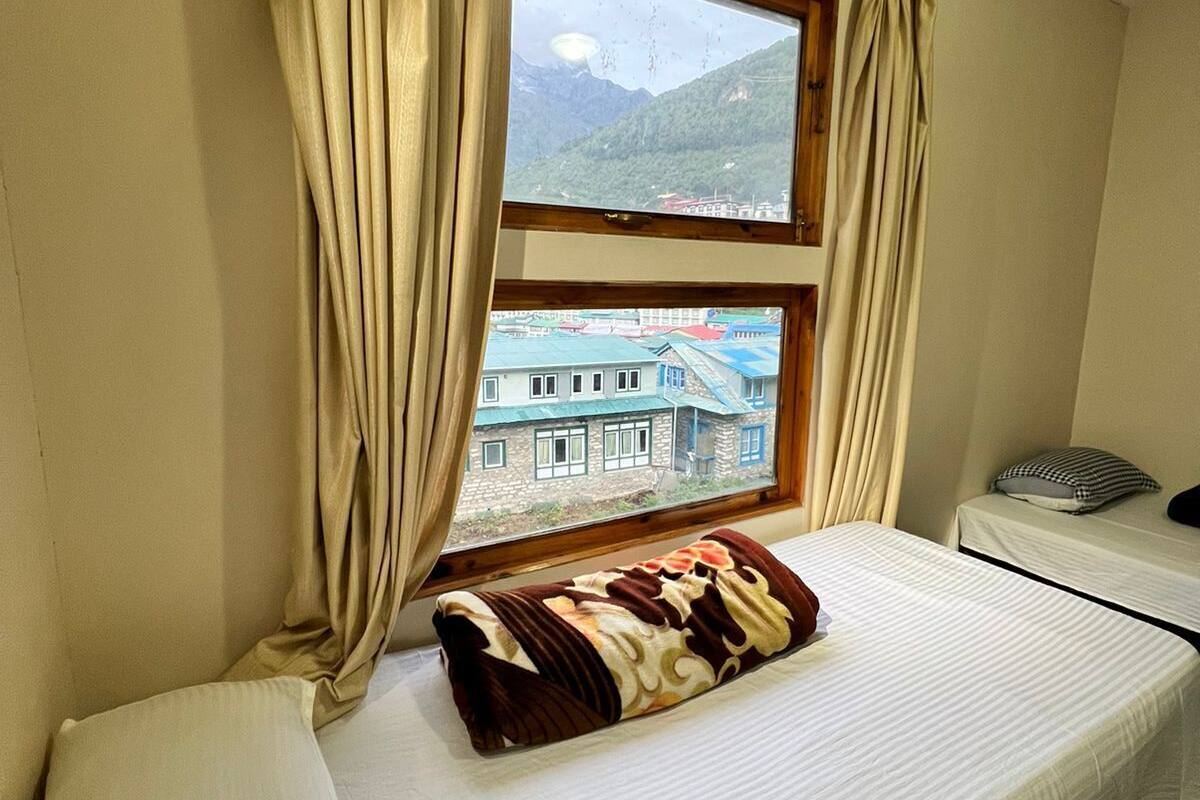 Una habitación con una cama, una ventana con cortinas, vistas a la montaña y una mesita con un cojín.