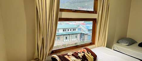 Una habitación con una cama, una ventana con cortinas, vistas a la montaña y una mesita con un cojín.