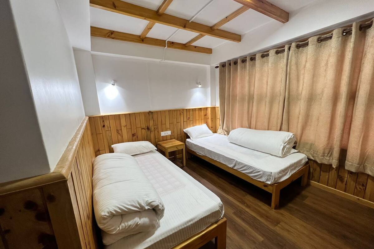 Una habitación con dos camas de madera, una mesita de madera y un techo con vigas a la vista.