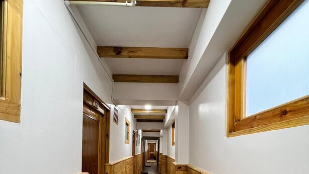A narrow hallway with wooden paneling and a wooden floor, leading to multiple doors at the end. - Hotel Camp De Base (Namche Bazar)