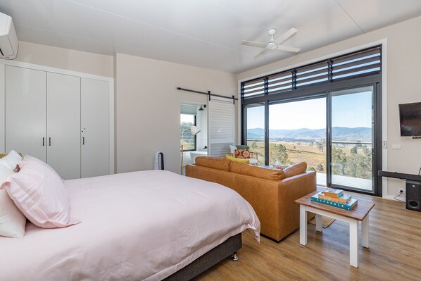 A bedroom with a large bed, a sofa, a small table with books, a ceiling fan, and a large window with a view of the countryside. - "another Secret Place" (Gloucester)