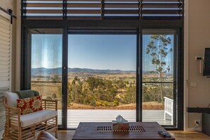 A room with a large sliding glass door leading to a deck, a wicker chair with a cushion, a wooden table with a tissue box and remote control, and a TV mounted on the wall. - "another Secret Place" (Gloucester)