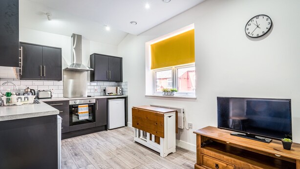 Une cuisine moderne avec des meubles de couleur sombre, une hotte de cuisine en acier inoxydable, un four encastré et un meuble TV en bois.