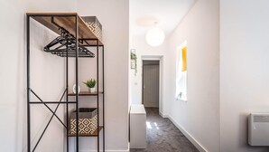Un couloir avec une étagère métallique, une porte blanche et un radiateur.
