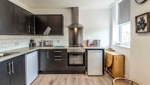 A modern kitchen with dark cabinets, a stainless steel range hood, a built-in oven, and a small refrigerator. - 1 bed Apartment near Liverpool Lime street (Old Swan)