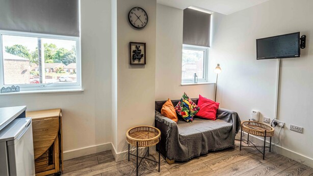 A modern room with a sofa, a small table, a clock, and a television. - 1 bed Apartment near Liverpool Lime street (Old Swan)